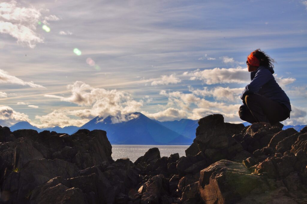 Mujer observa el paisaje de montañas y lago desde una formación rocosa al atardecer en el Parque Nacional Nahuel Huapi.