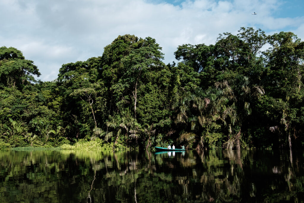 Bote con personas navegando por un río en medio de la selva amazónica, rodeado de árboles y reflejos en el agua.