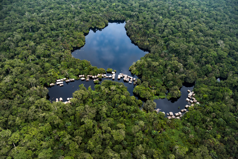 Vista aérea de un lago rodeado de selva amazónica con casas flotantes agrupadas en sus orillas.