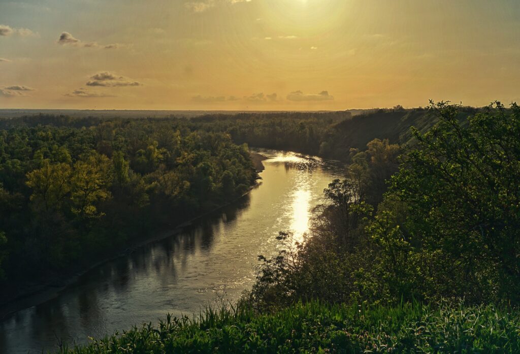 Vista panorámica de un río serpenteante rodeado de vegetación densa y colinas, iluminado por la luz dorada del atardecer.